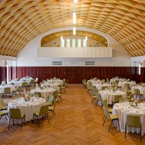 Großer Saal mit runden Tischen und stilvollem Holzdekor.